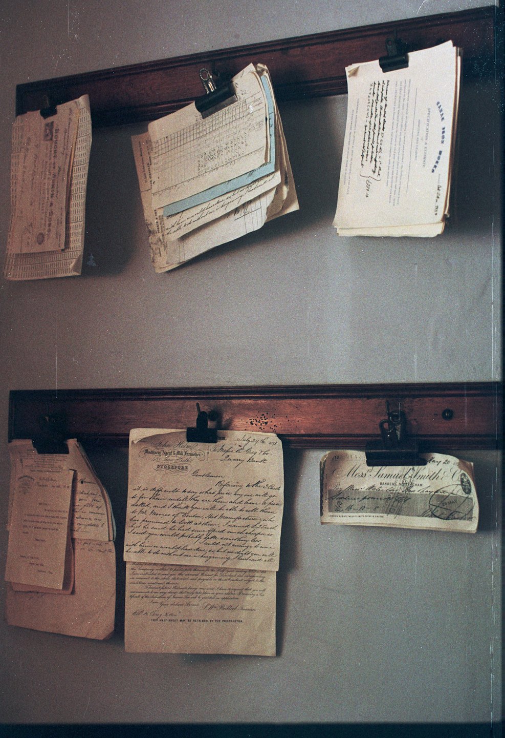 Documenti e lettere d'epoca appesi a binari di legno su una parete.