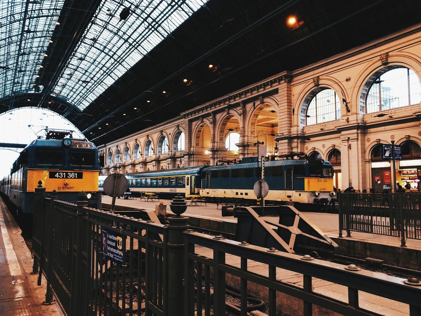 Due treni in una grande stazione ferroviaria europea sotto un tetto di vetro.