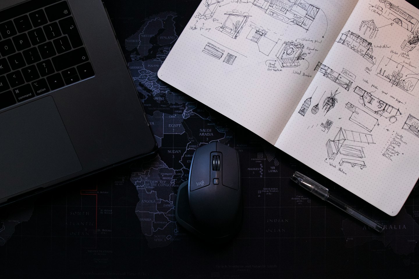 Scrivania con laptop, schizzi su taccuino e mouse su una mappa del mondo.
